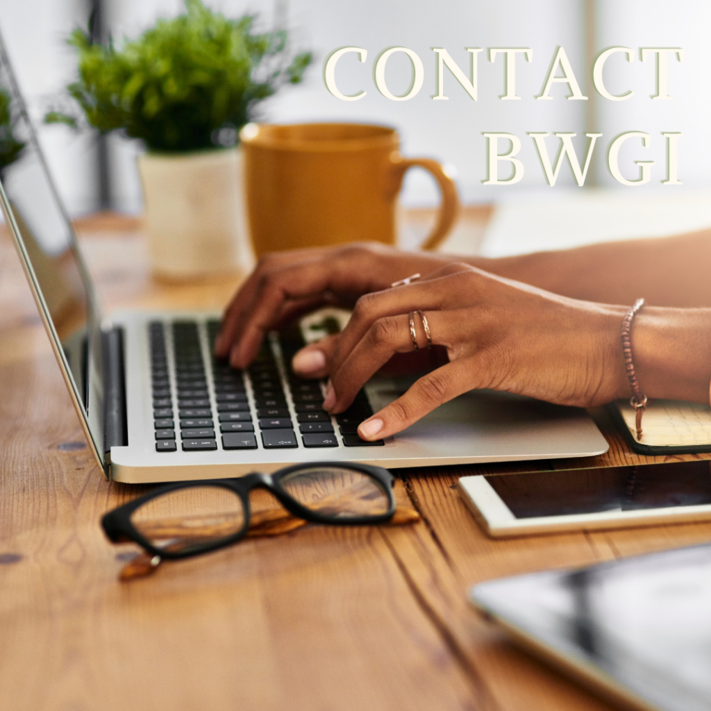 black glasses and iphone in foreground. medium brown hands type on computer in mid ground. coffee cup and plant in background