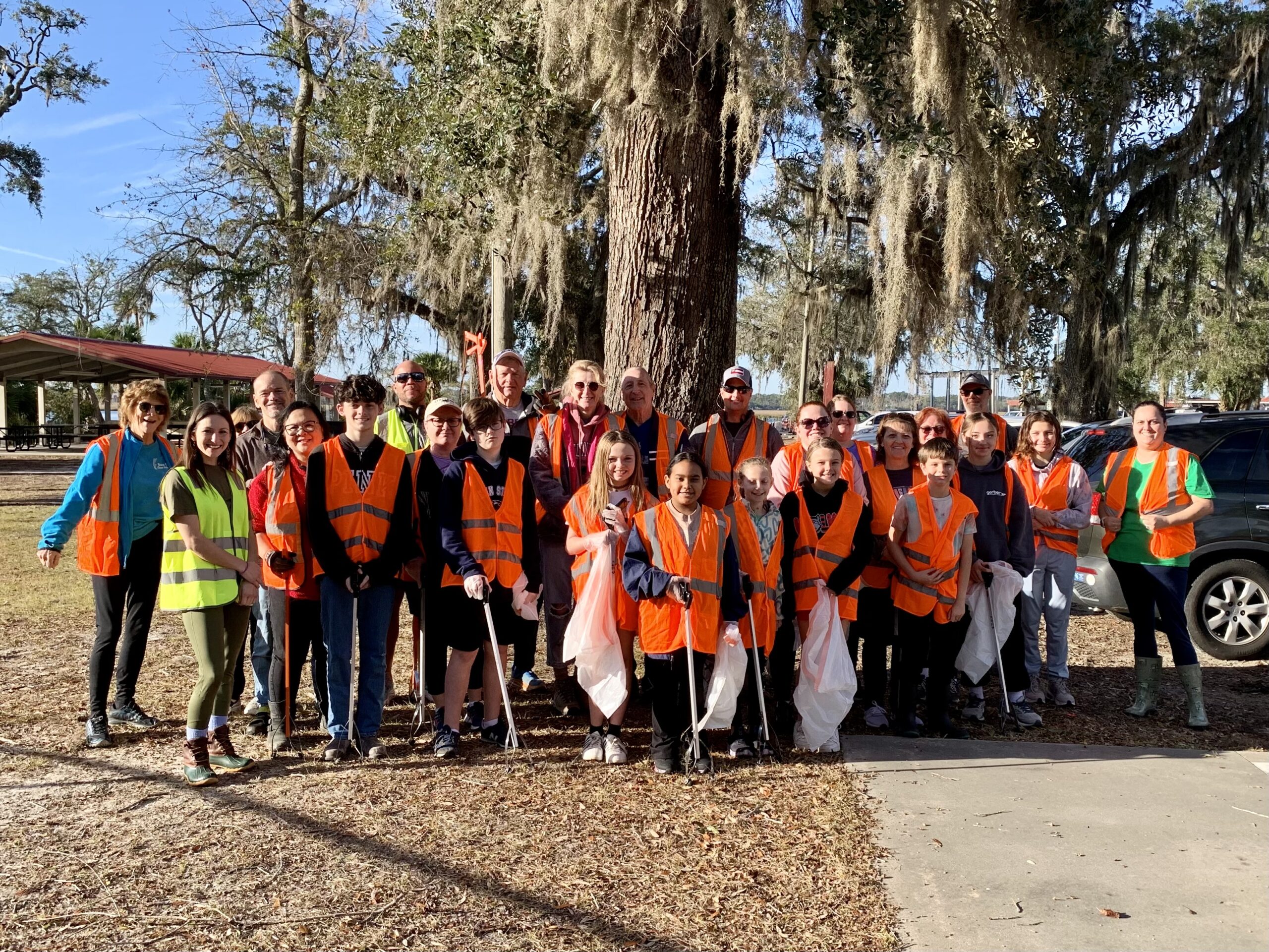 group of people wearing orange or yellow vests and holding trash bags stand in front of a live oak tree group of people wearing orange or yellow vests and holding trash bags stand in front of a live oak tree